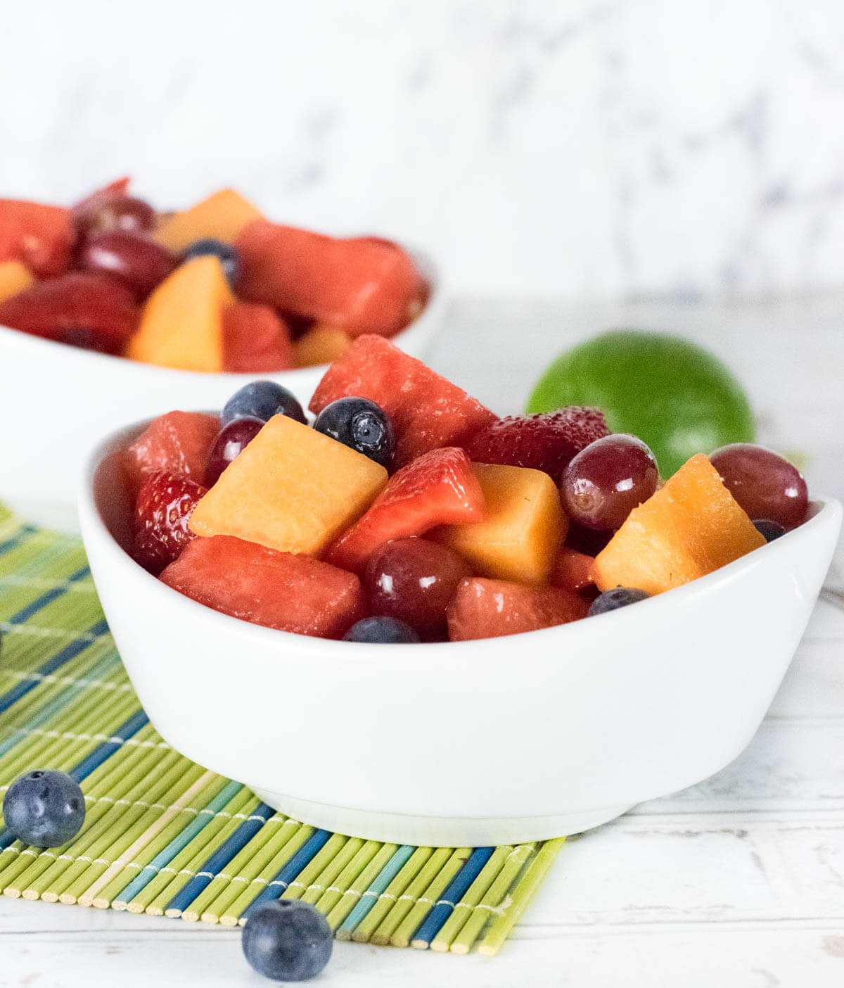 Fruit salad in white bowl on green mat.