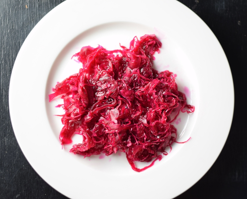 Homemade fermented sauerkraut on a white plate with black background.