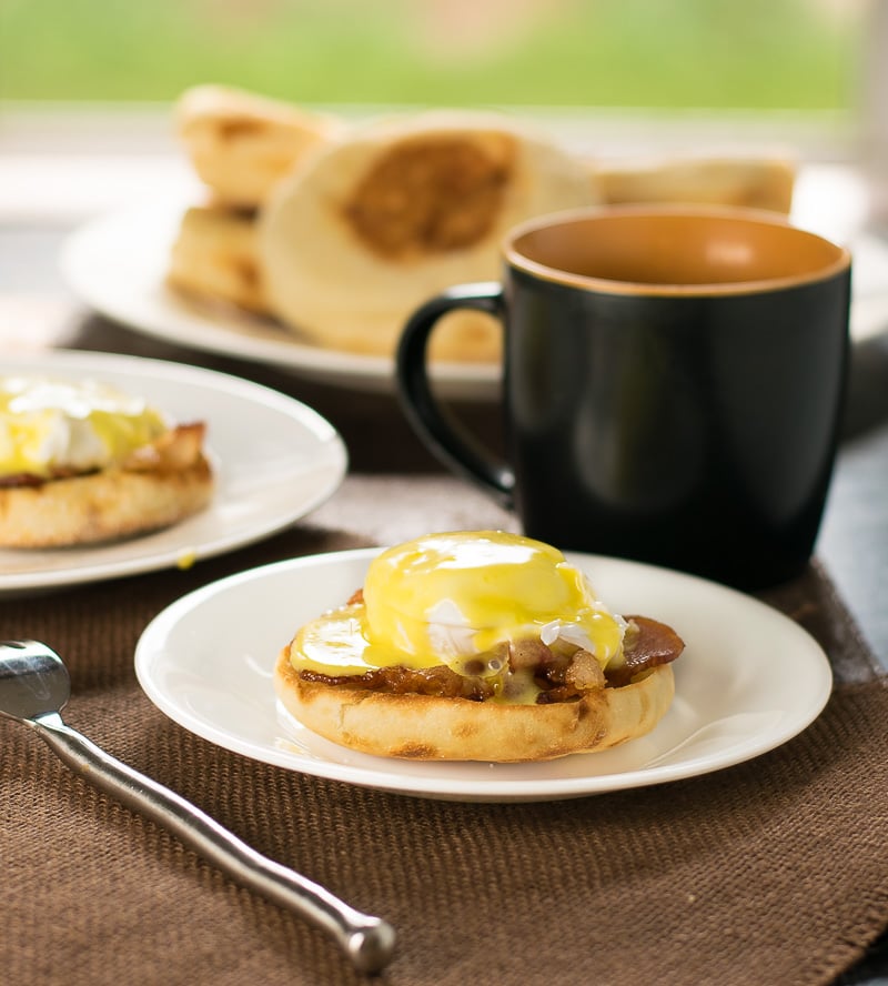 Bacon and Eggs Benedict on white plate with cup of coffee.