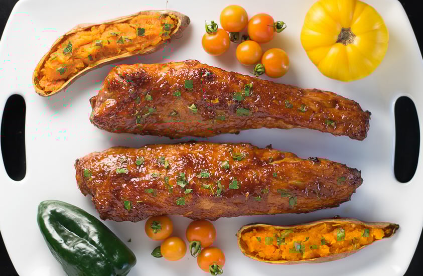 Two Cherry Chipotle BBQ Sauce Glazed Pork Tenderloins with sweet potatoes on tray.