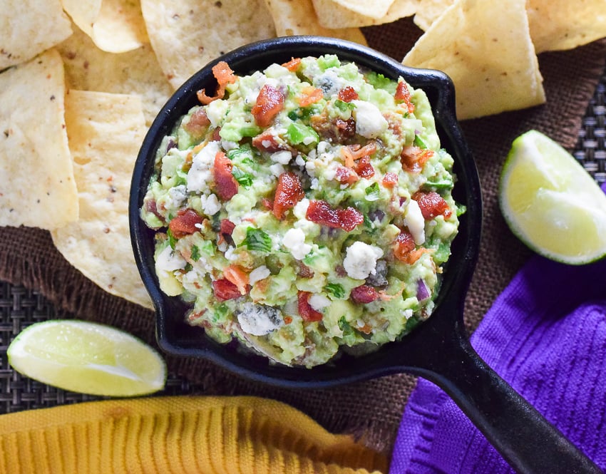 Blue Cheese and Bacon Guacamole Dip recipe in a cast iron dish surrounded by tortilla chips.