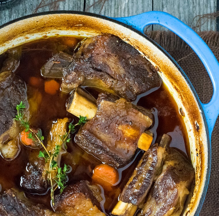 Beer Braised Short Ribs cooking in a blue Dutch Oven.