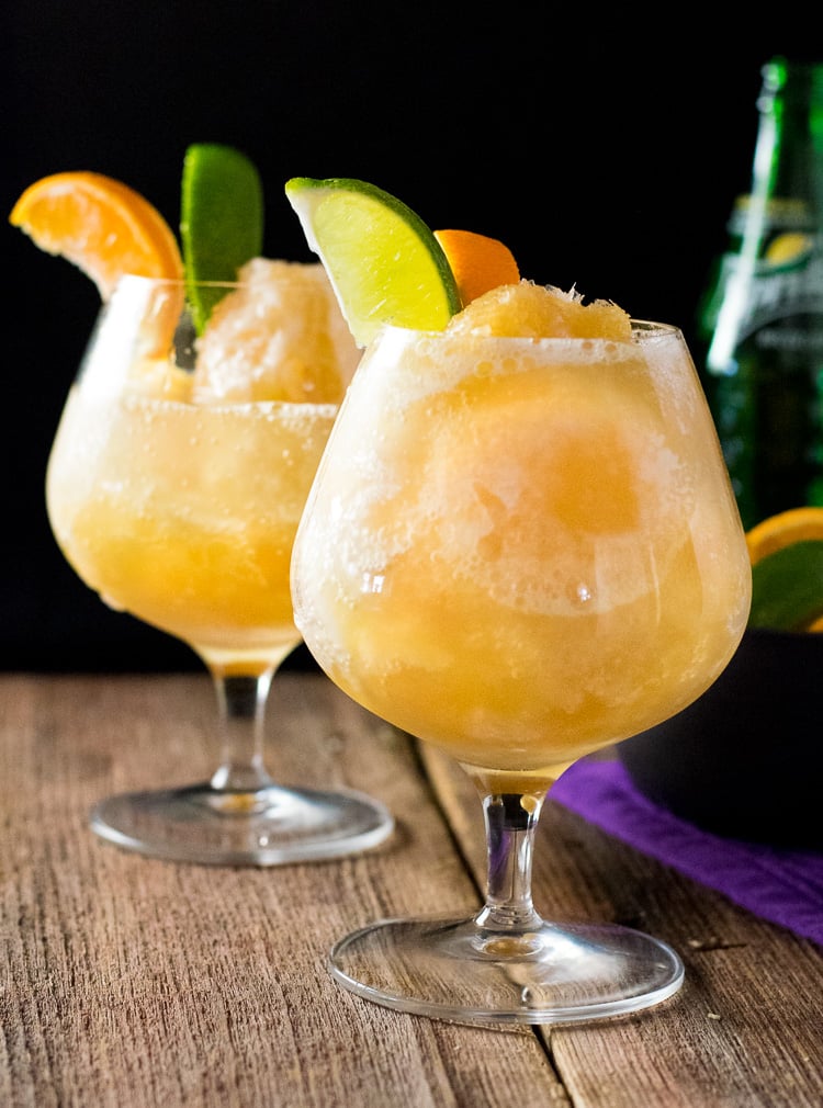 Two brandy slushes served with orange and lime slices.