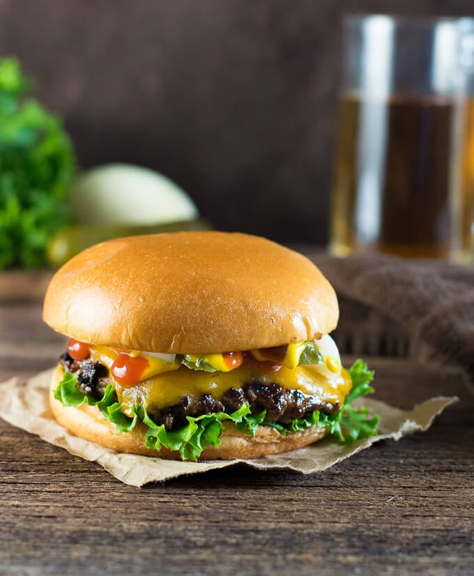 close-up view of a juicy cheese hamburger with ketchup, mustard, onions, and lettuce on a brioche bun