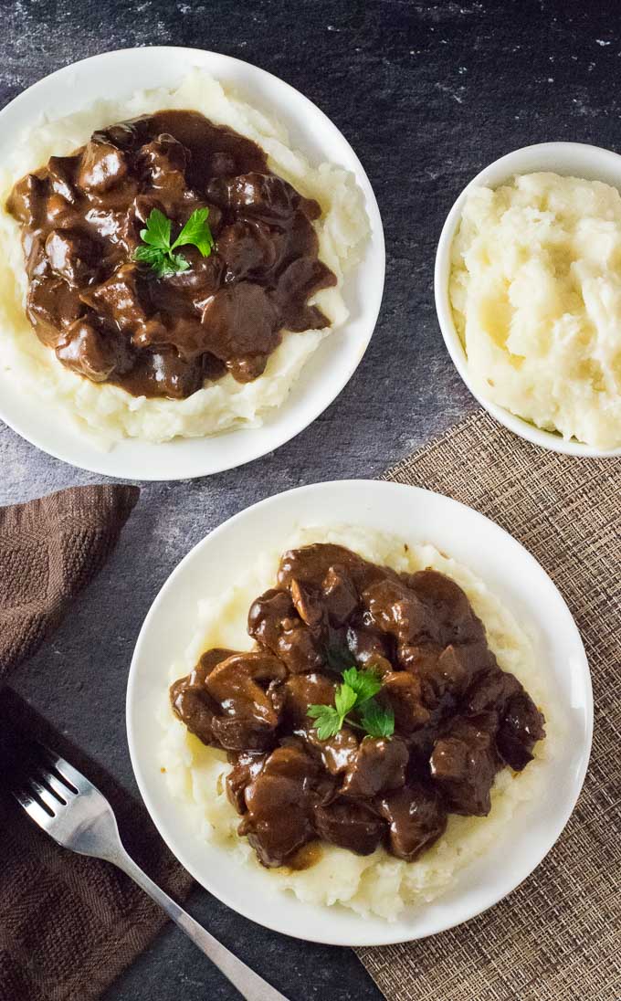Beef tips and gravy over mashed potatoes on two plates.