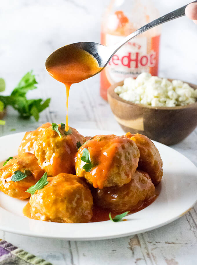 Chicken meatballs being drizzled with buffalo sauce on a white plate.