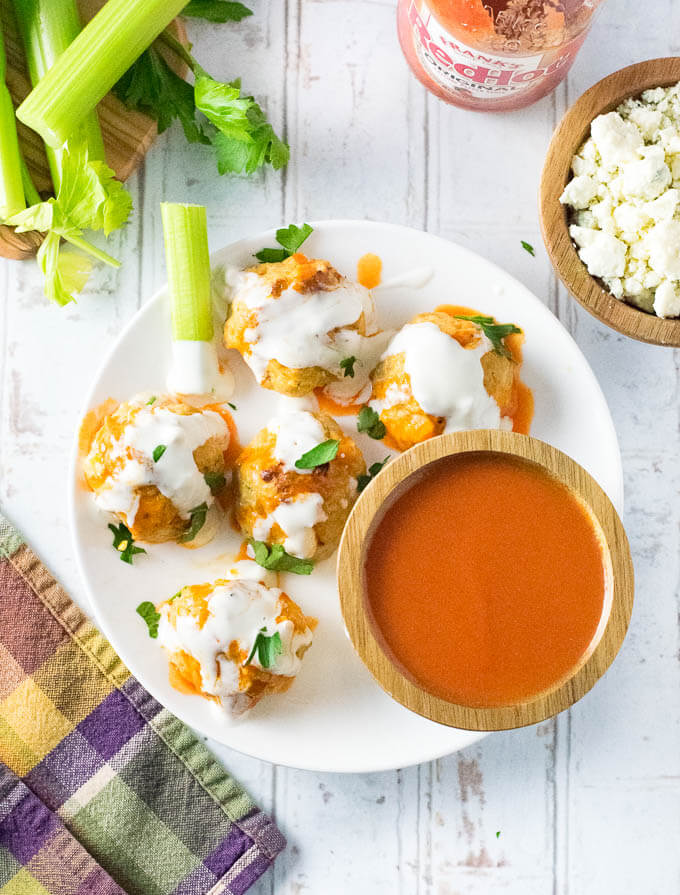 Buffalo Chicken Meatballs covered in dressing with a bowl of sauce sitting on a white plate.