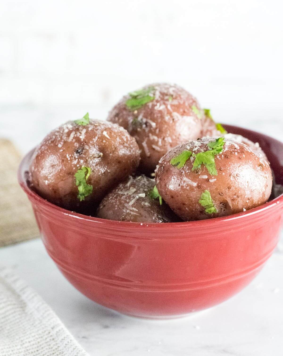 Boiled red potatoes in red bowl with Parmesan sprinkled on top.