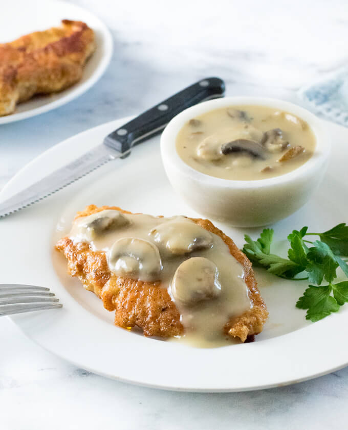 Chicken with mushroom gravy on a white plate with knife.