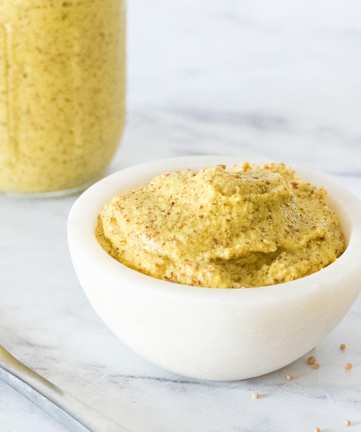 Close view of Dijon mustard in a white bowl with jar behind.