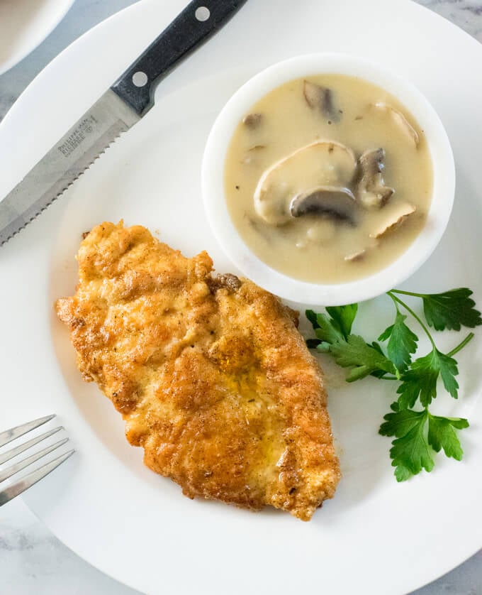 Lightly breaded chicken next to bowl of mushroom gravy.