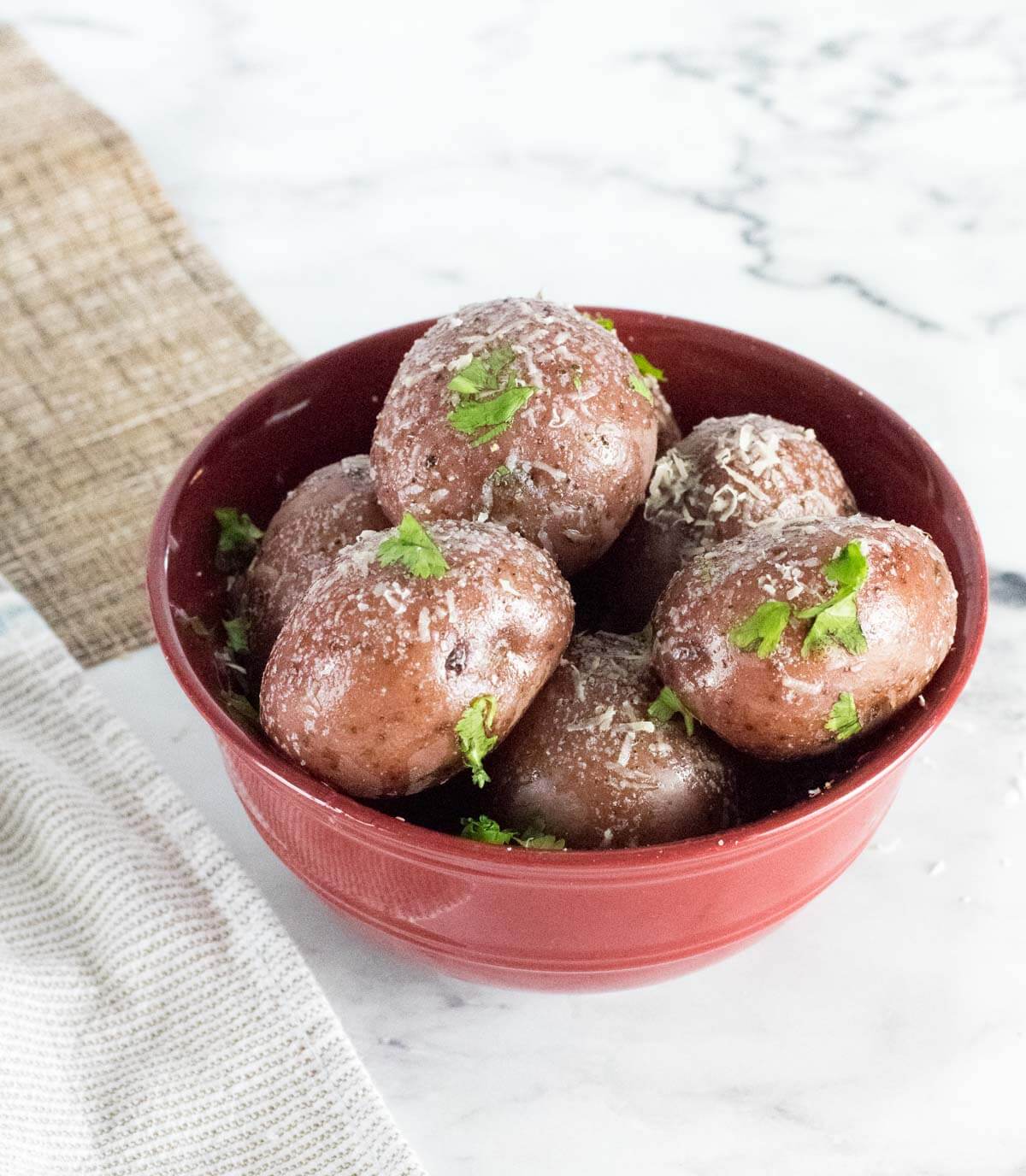 Red potatoes with butter and Parmesan in a bowl with white background.