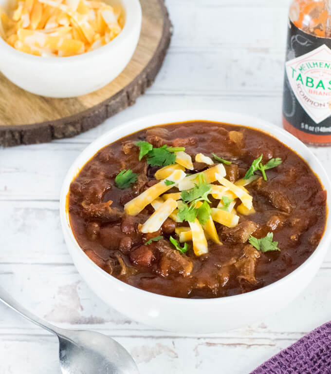 Shredded beef chili with cheese and hot sauce in background.