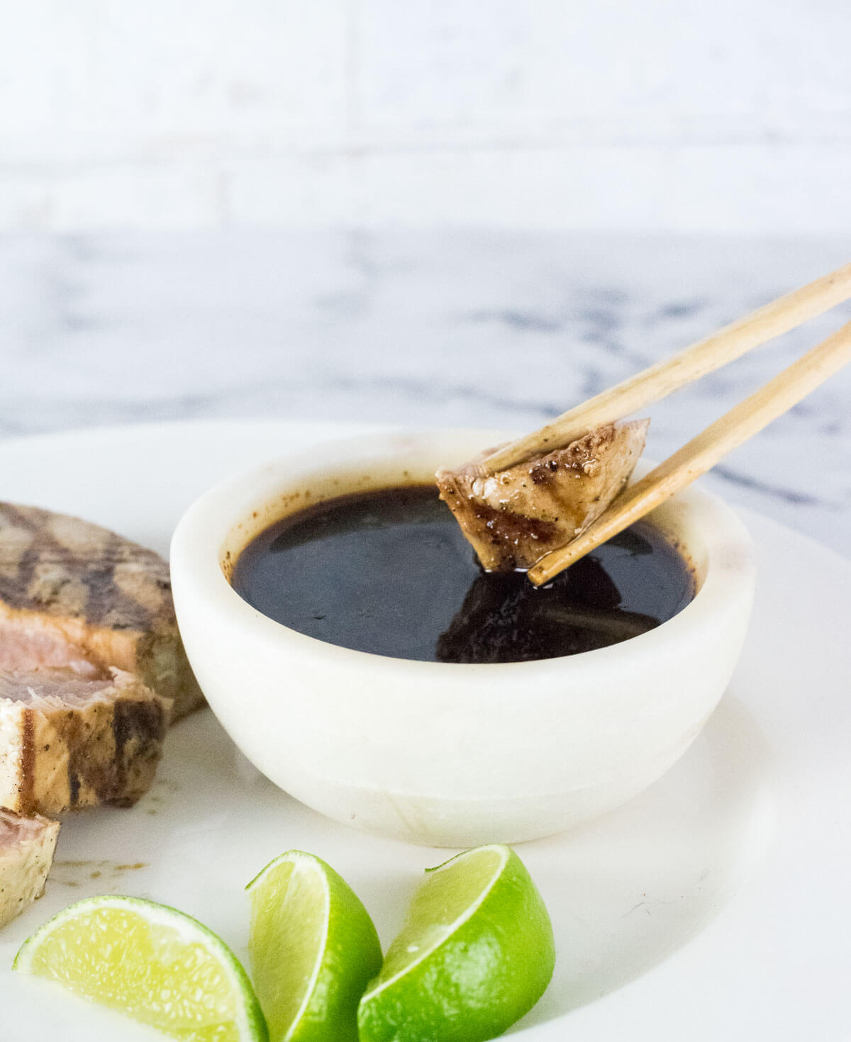 Grilled tuna being dipped into sauce.