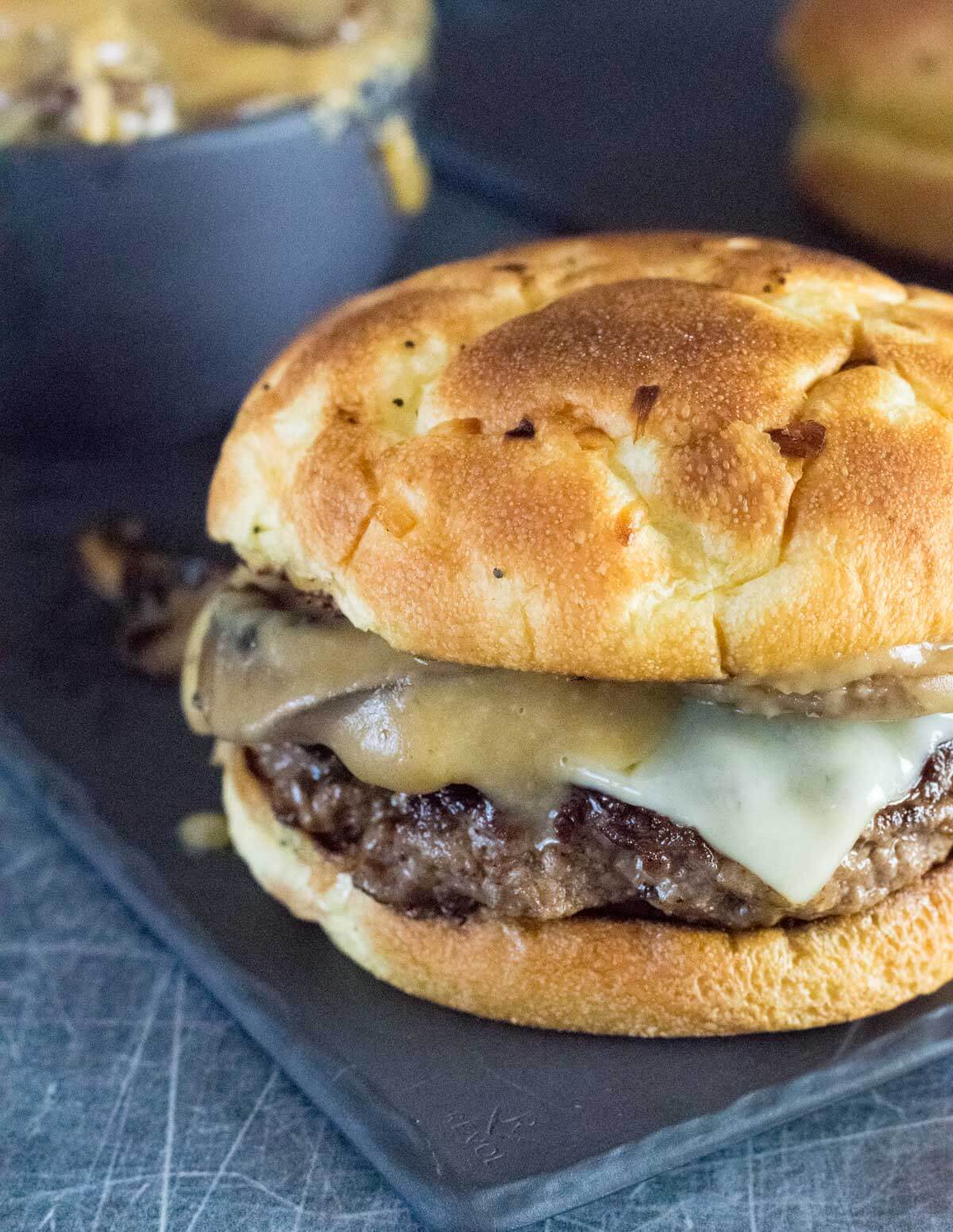 Homemade mushroom Swiss burger with gravy shown close up with gravy dripping off the side.