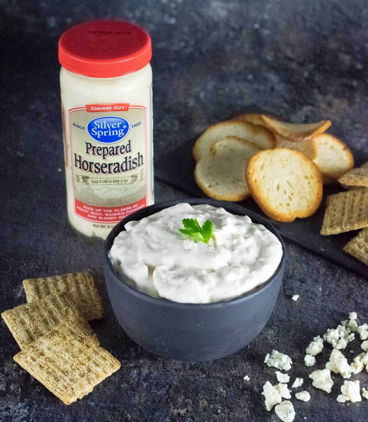 Bacon horseradish dip in bowl with horseradish bottle behind.