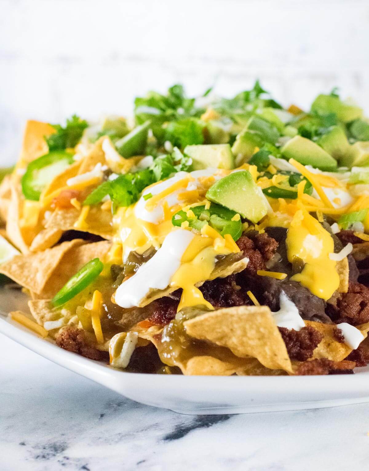 Chorizo nacho topped with avocado and cheese shown close up.