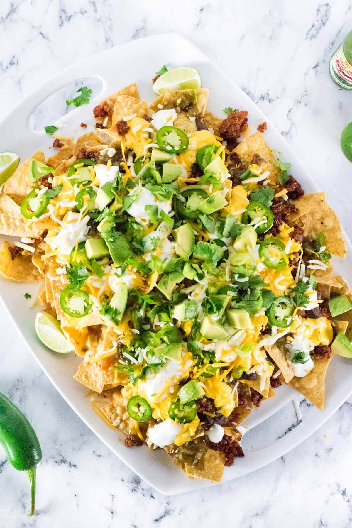 Chorizo nachos on a white platter with jalapeno set alongside.