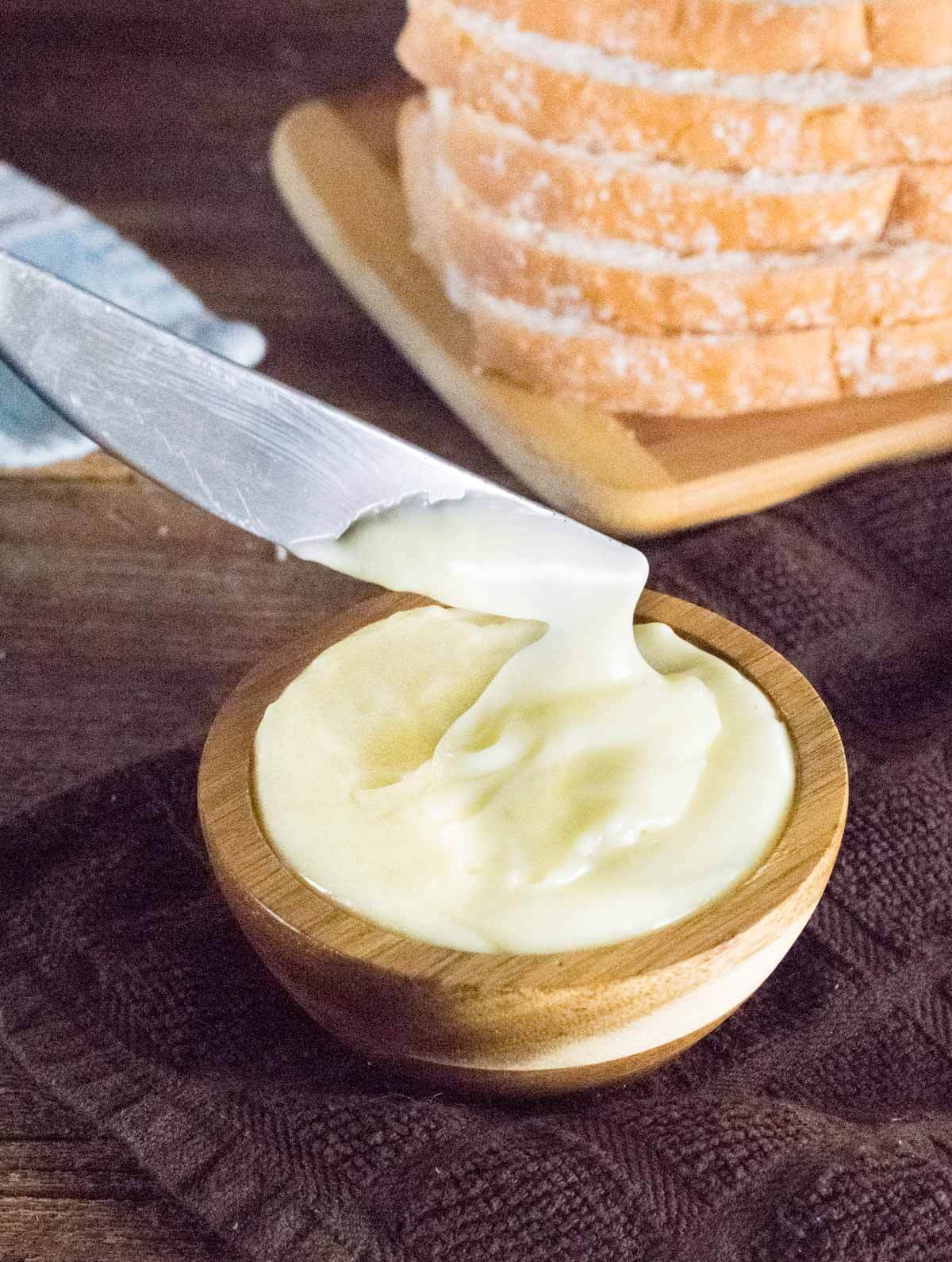 Homemade mayo in wooden dish, spread with knife.
