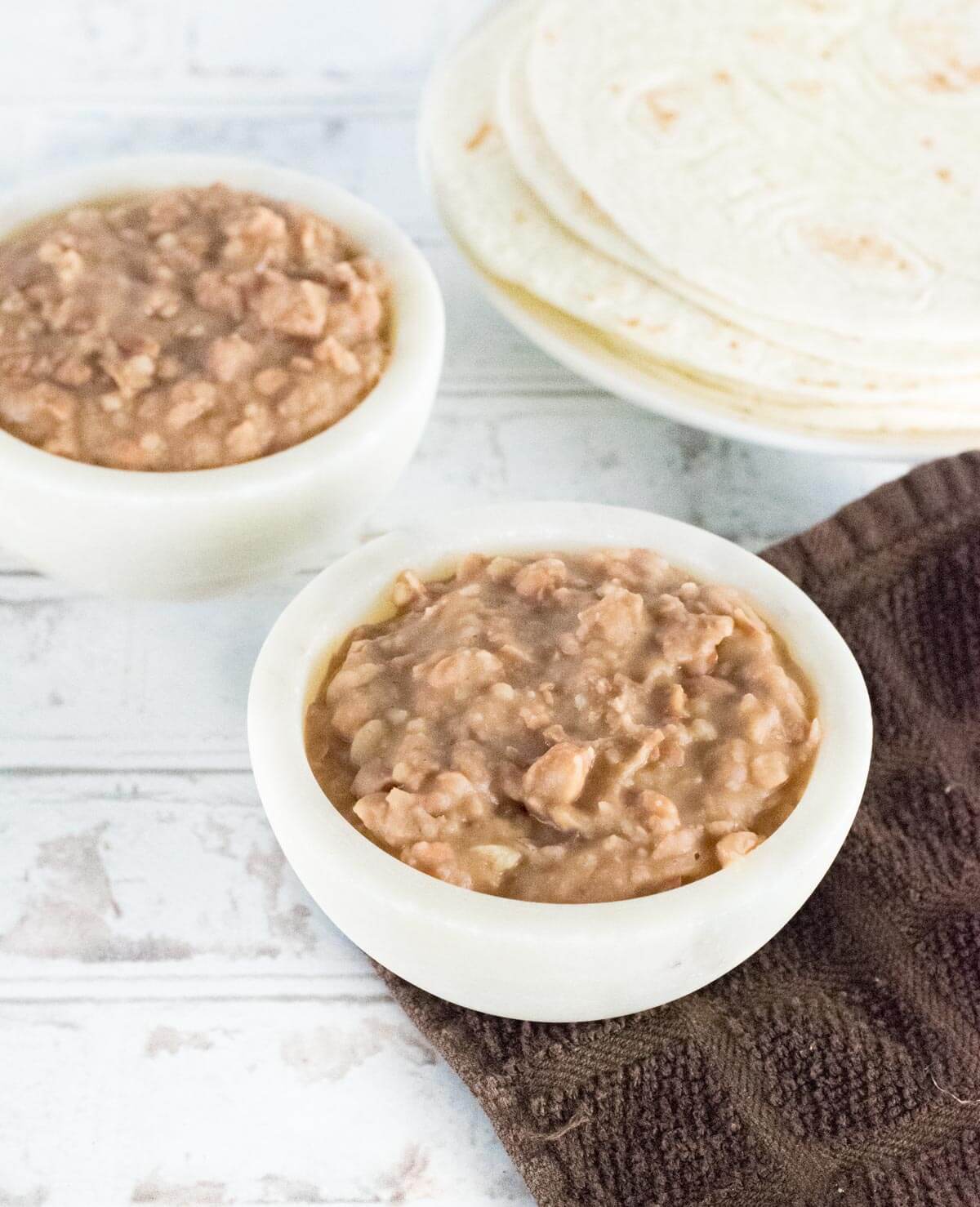 Two white bowls of homemade refried beans.