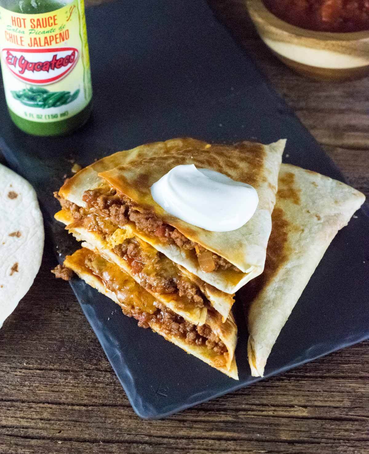 Ground beef quesadillas stacked on top of each other and topped with sour cream.