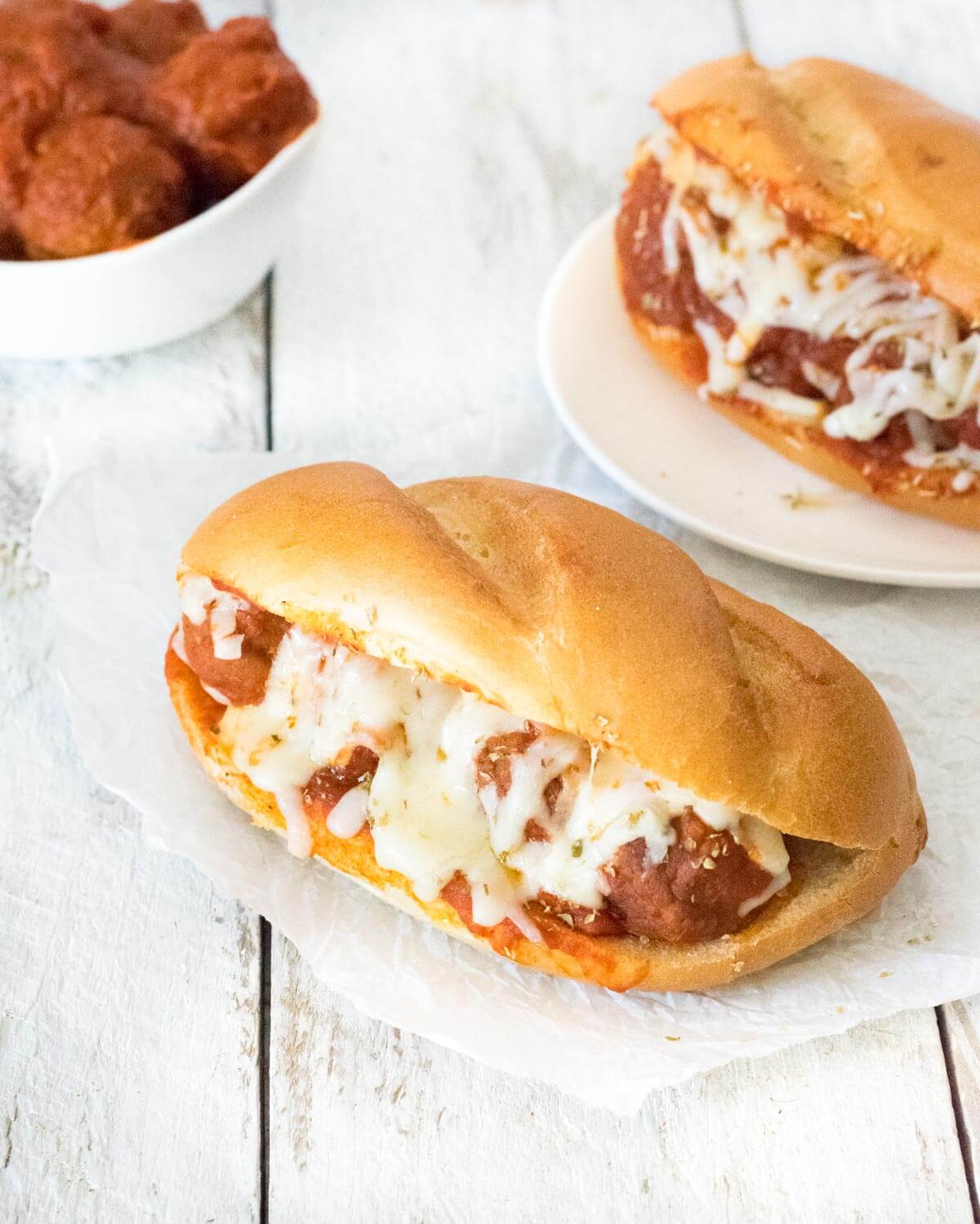 two meatball subs and a dish of meatballs.