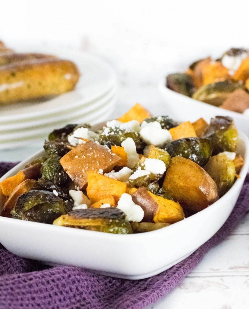 Sweet potatoes and Brussels sprouts topped with feta and served in a white dish.