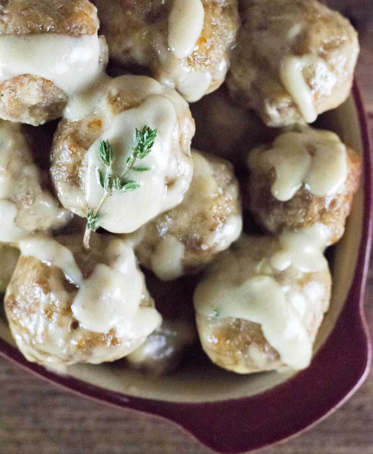 Meatballs in dish with gravy topped with thyme.