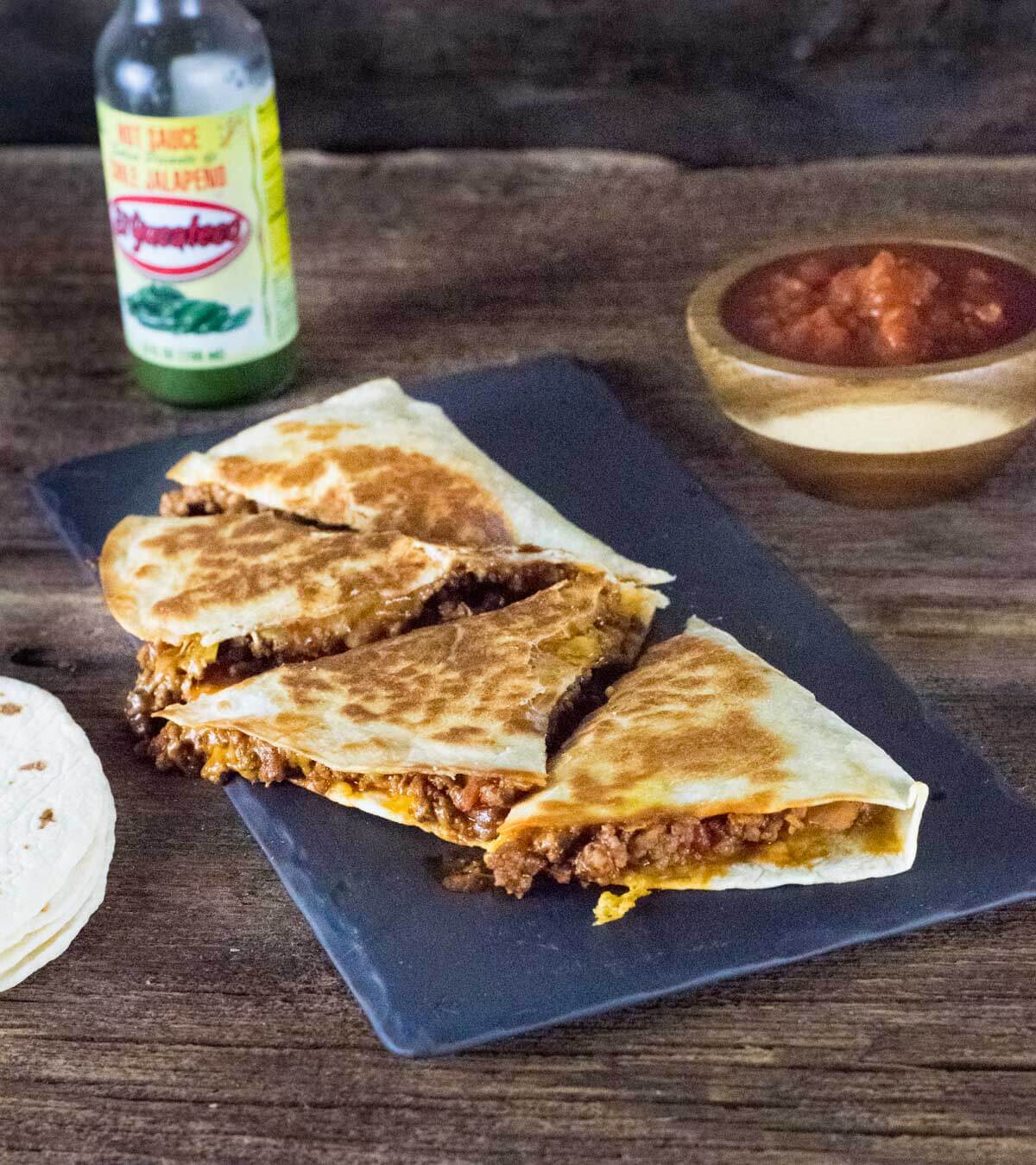 quesadilla on black tray with hot sauce.