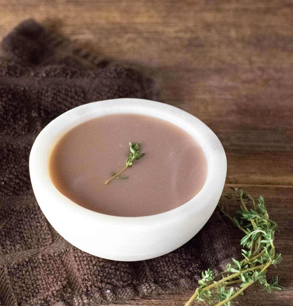 Red wine onion gravy in white bowl on brown towel.