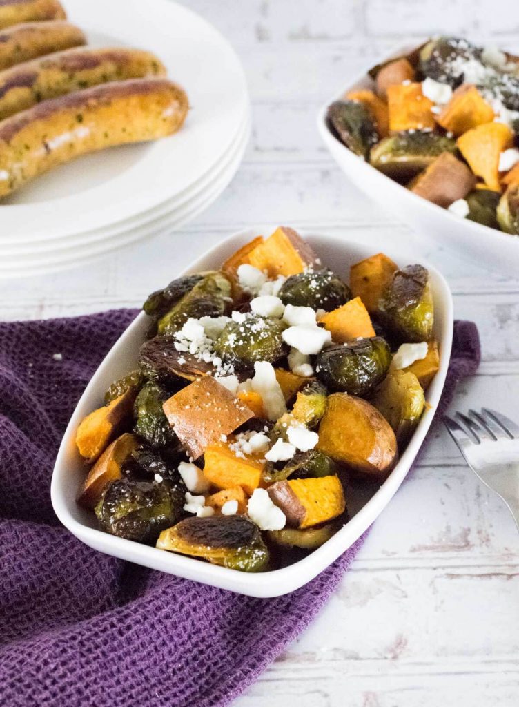 Roasted Sweet potatoes and Brussels sprouts with feta in dish on purple towel.