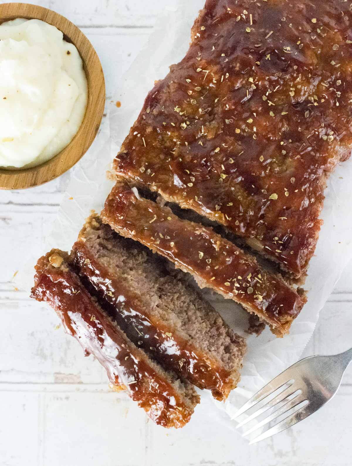 Sliced sausage meatloaf viewed from above with mashed potatoes alongside.