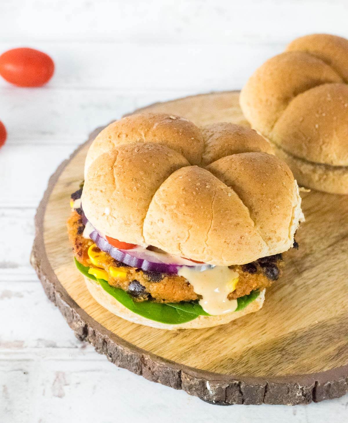Sweet potato black bean burger toppings and bun with sauce dripping down.