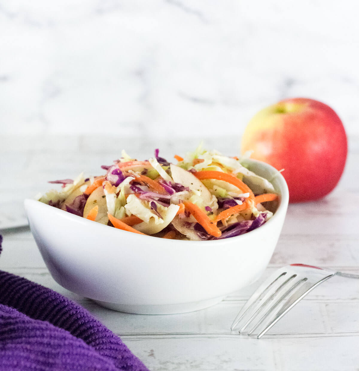 Apple Cider Vinegar Coleslaw in white bowl next to purple towel.