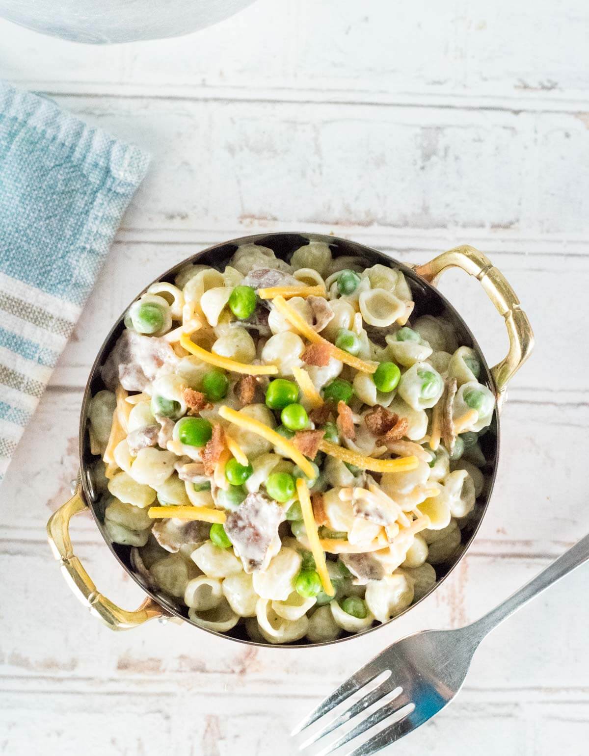Bacon and Pea Pasta Salad topped with cheese in copper bowl.