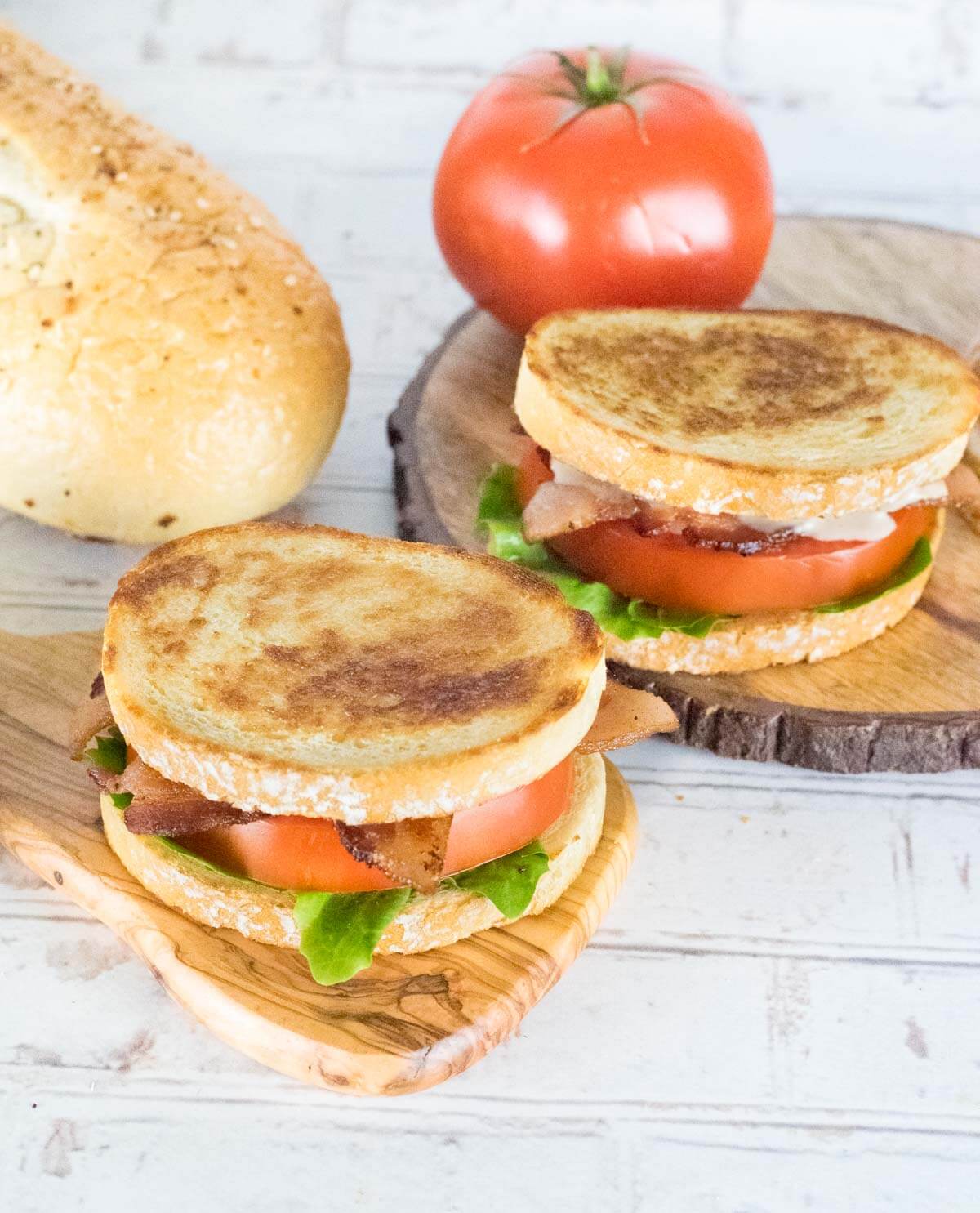 Two Gourmet BLTs with fresh bread on wooden trays.