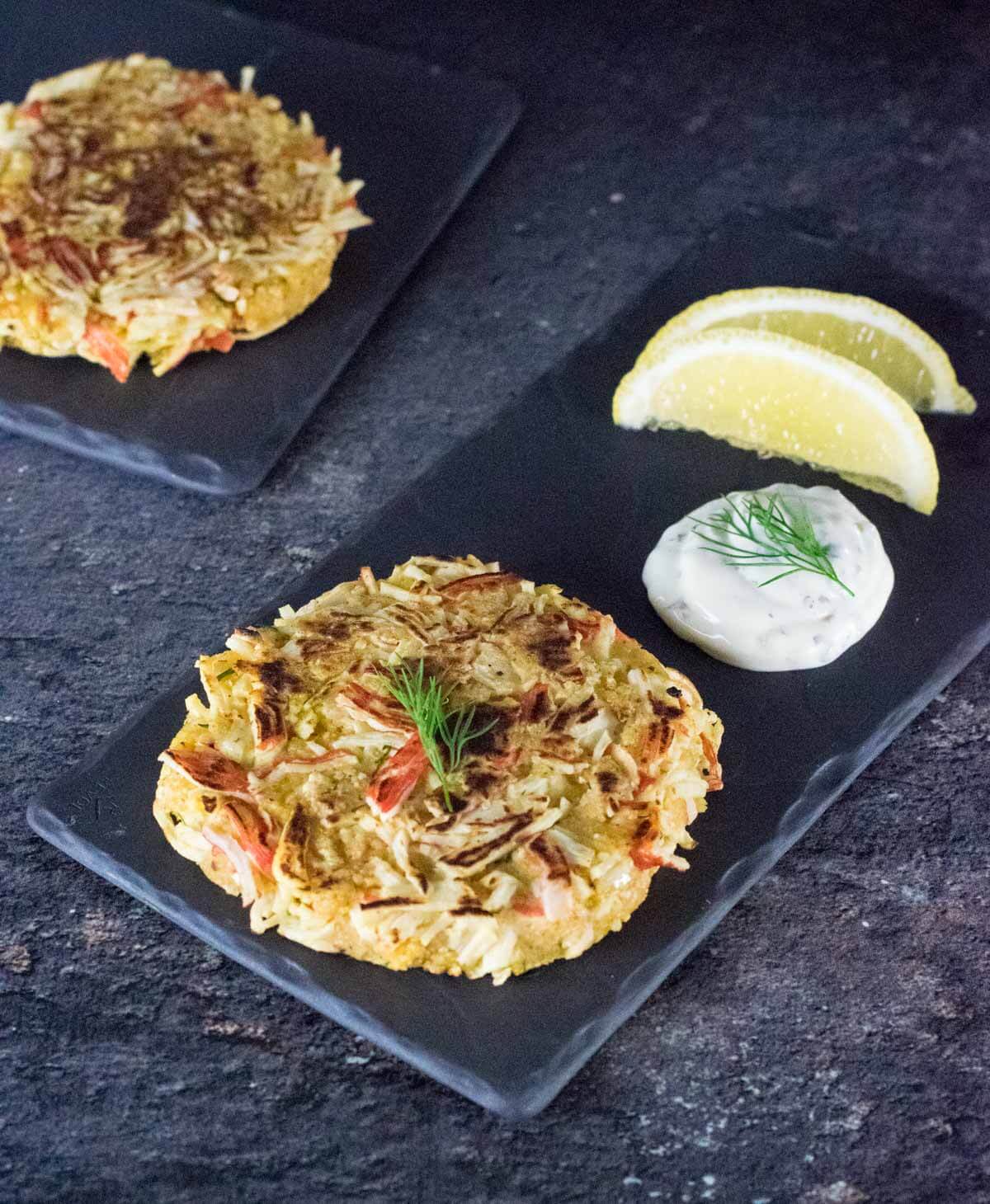 Two Imitation crab cakes and tartar sauce on stone.