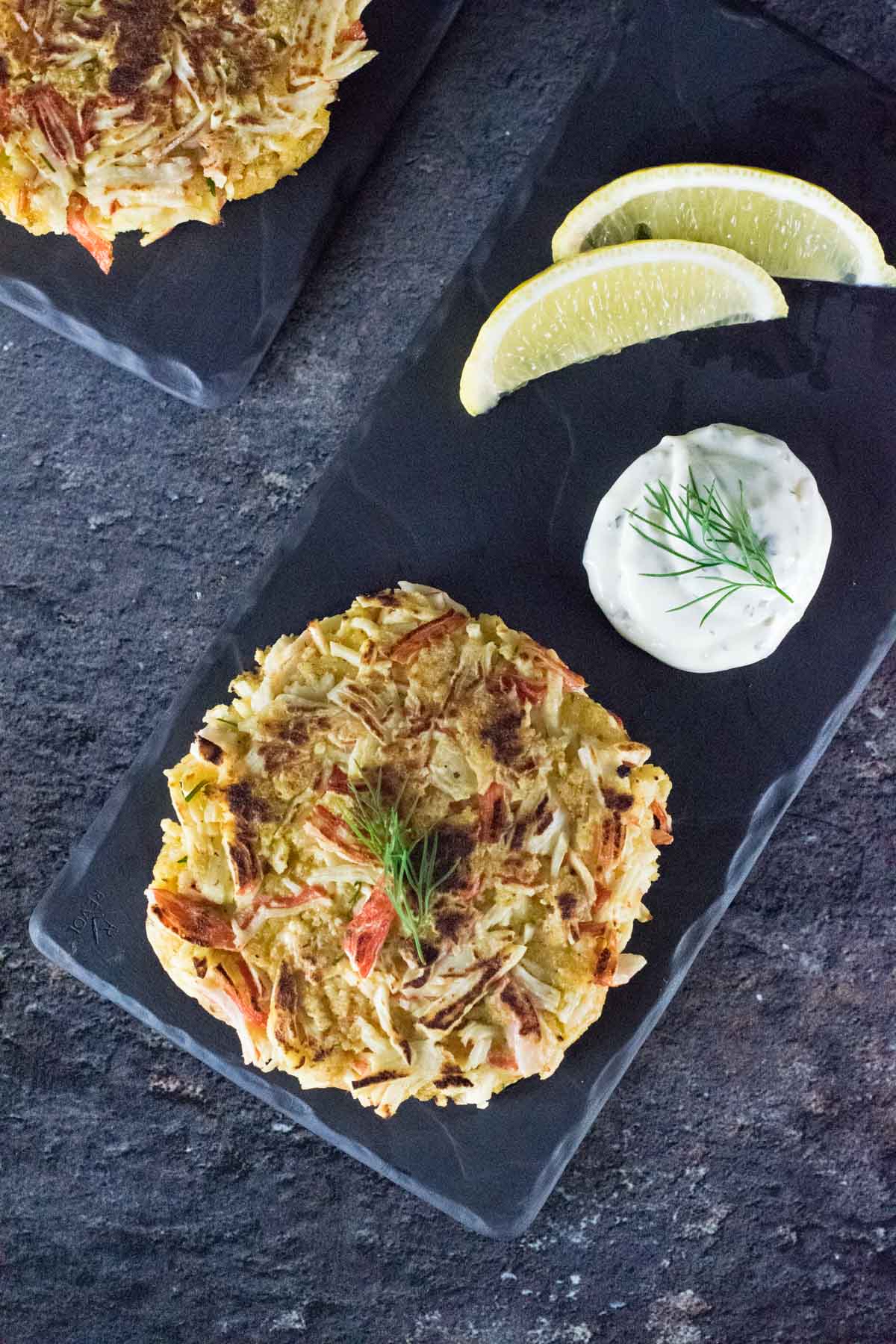 Imitation crab cakes on black tray with lemon wedges.