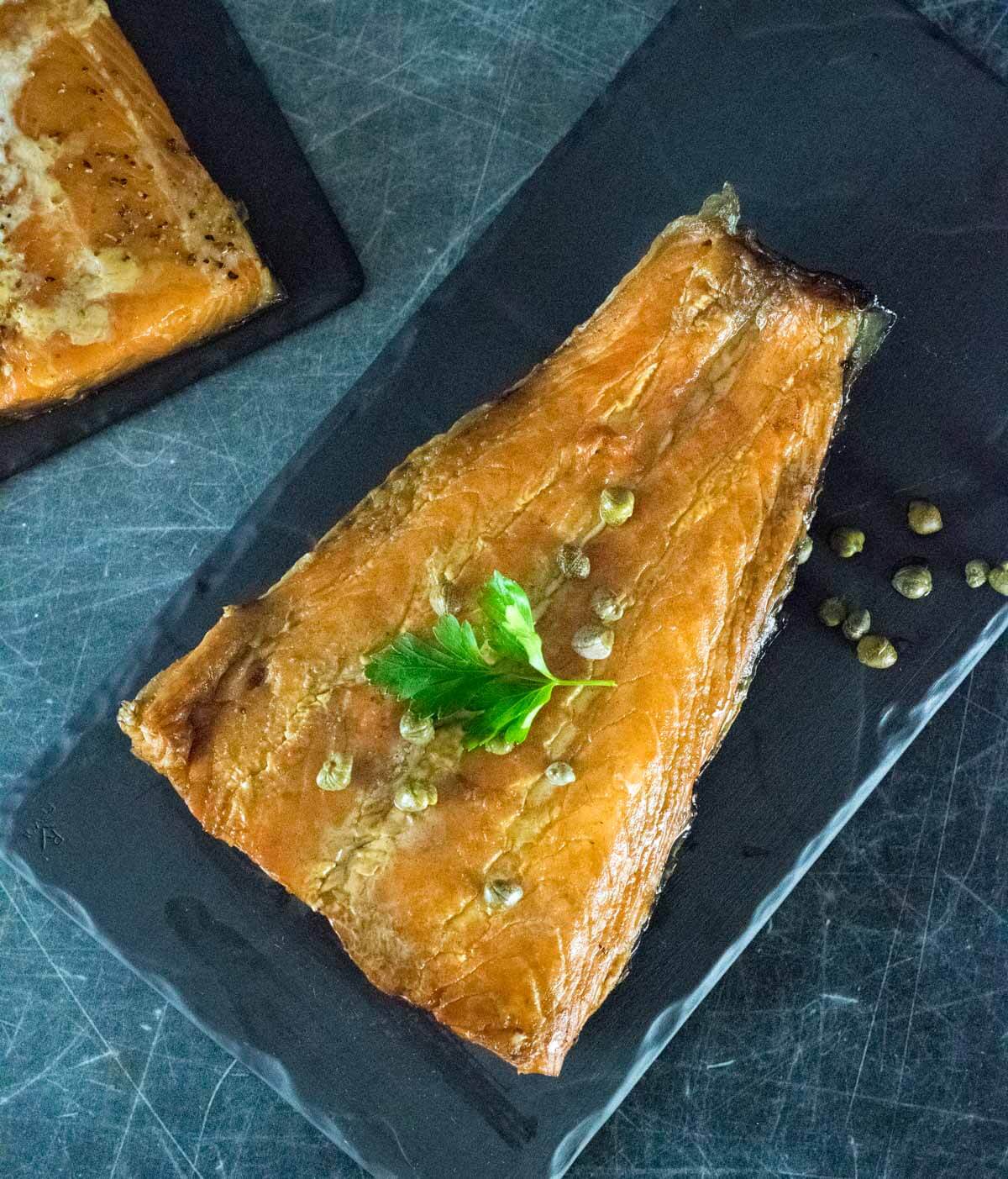 Smoked salmon fillet on a platter with parsley leaf.