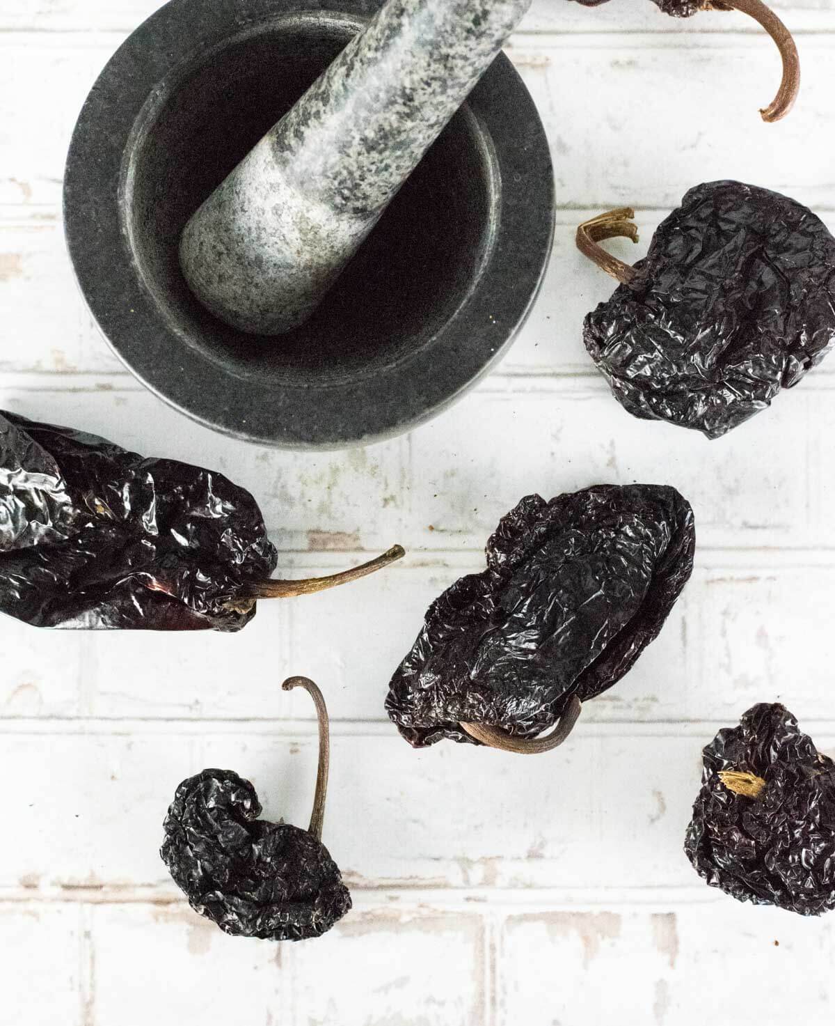 Dried ancho chiles sitting by mortar and pestle.