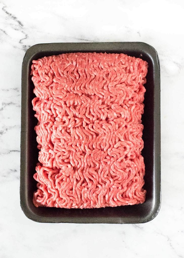 Raw hamburger in black container.