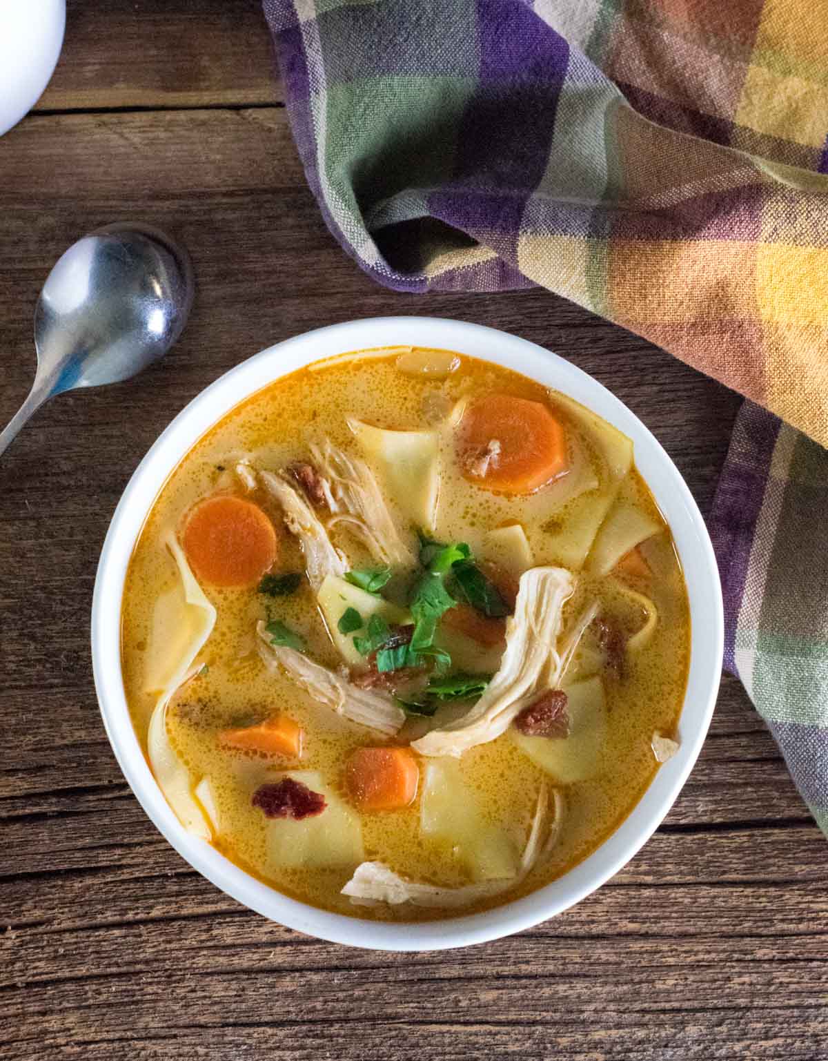 Spicy Chicken Noodle Soup in white bowl with spoon and towel alongside.