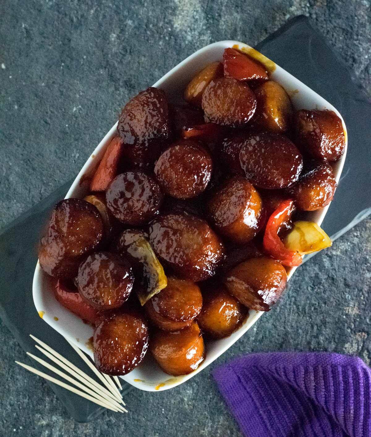 BBQ Smoked Sausage in white dish with peppers and onion.