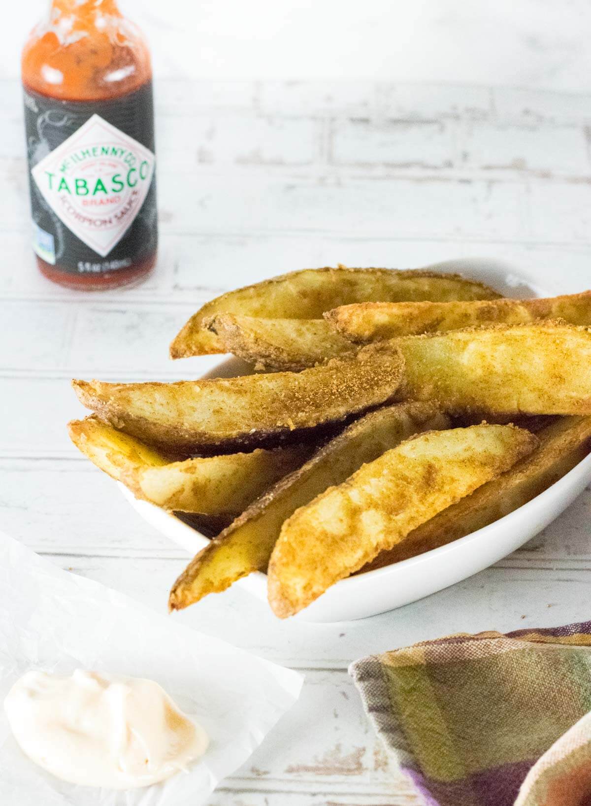 Cajun potatoes in a white dish with hot sauce shown behind.