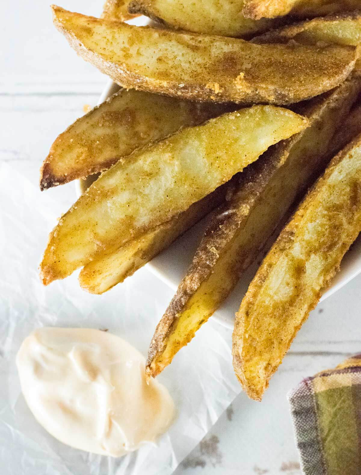 Cajun potato wedges with dipping sauce on wax paper.