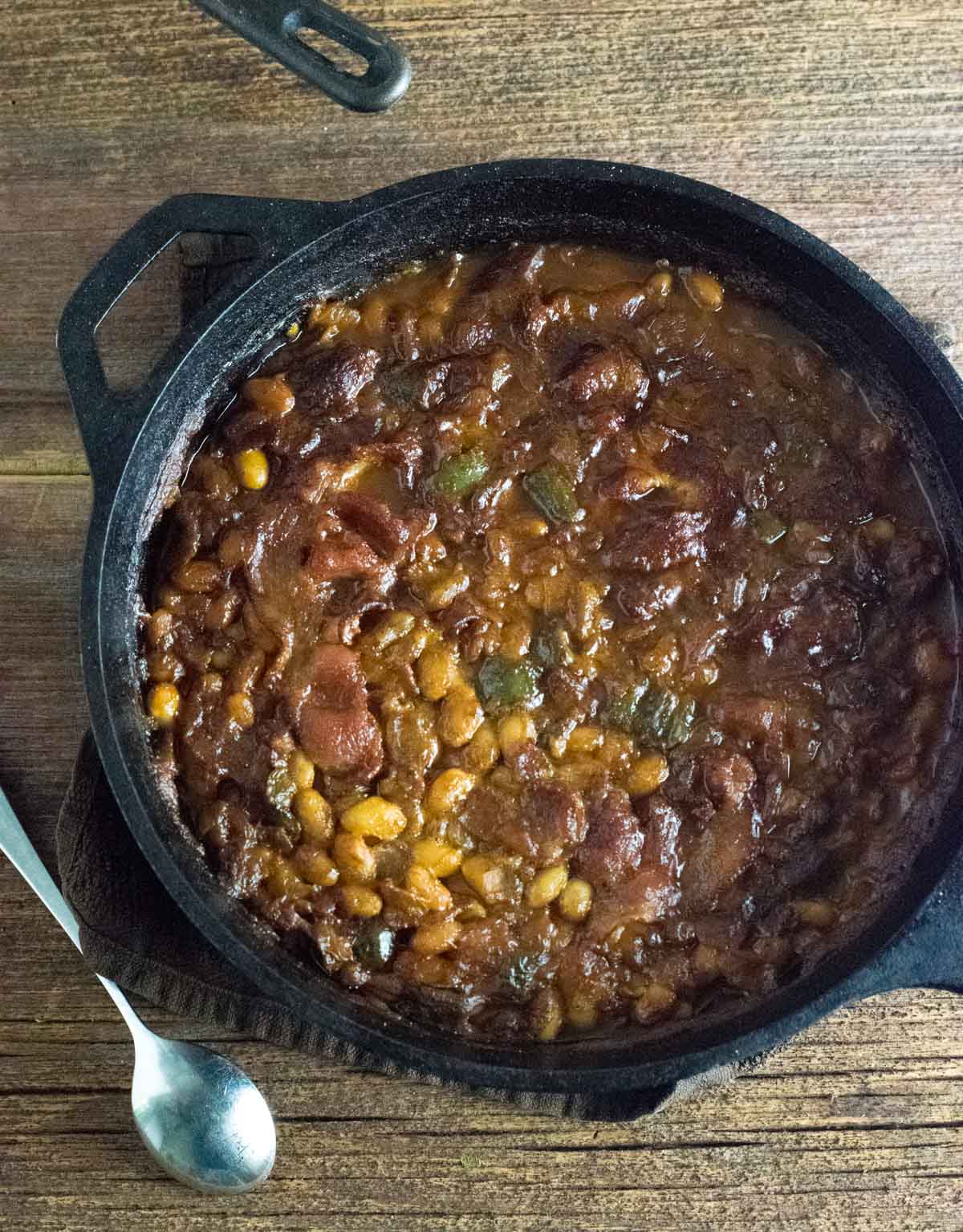 Pot of grilled Baked Beans resting on wooden board.
