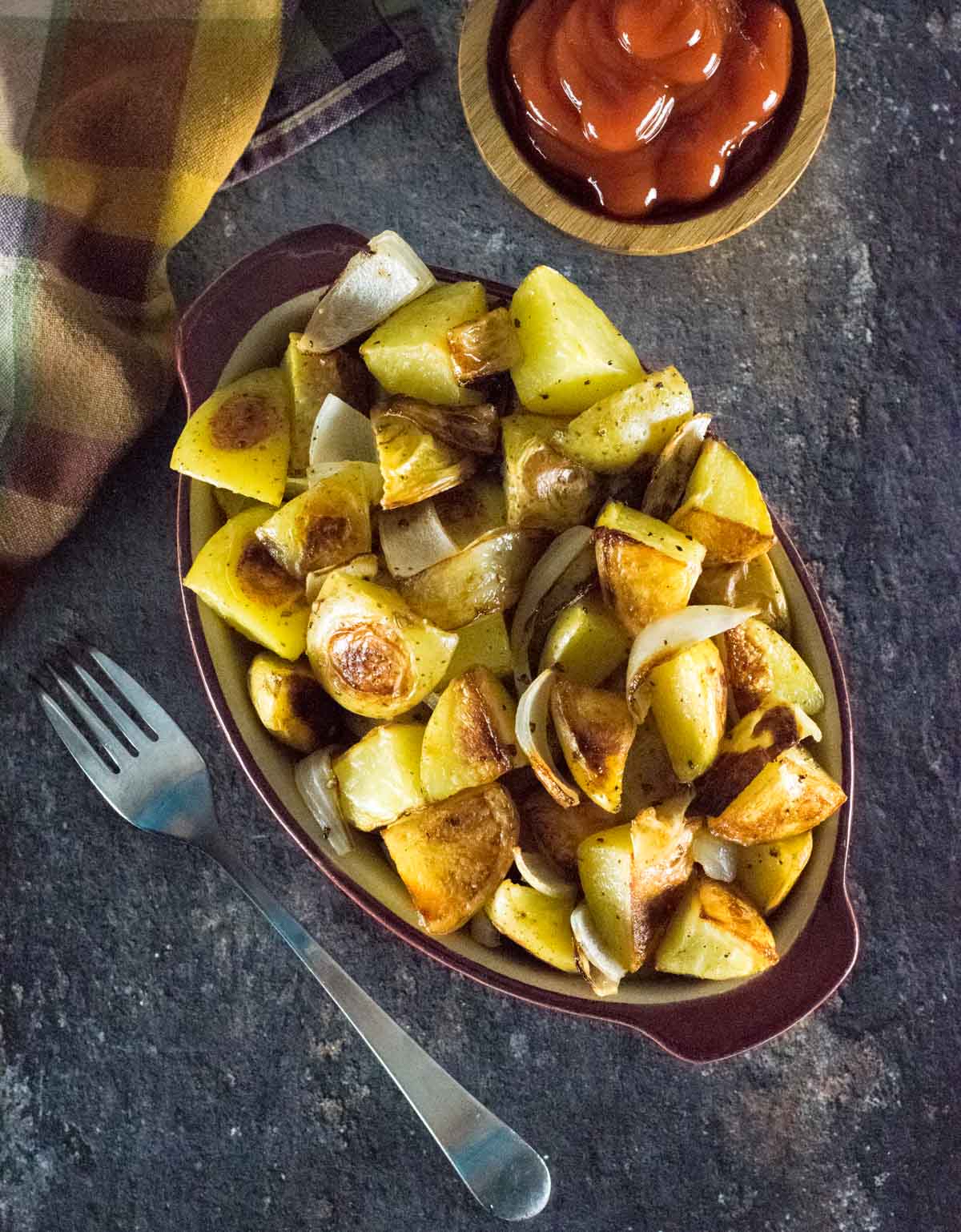 Roasted potatoes and onions shown from above with fork and kitchen towel alongside.