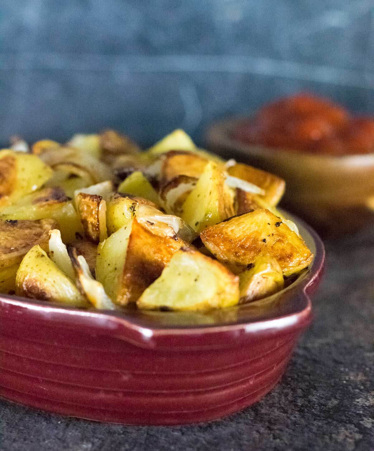 Roasted potatoes and onion in red bowl.