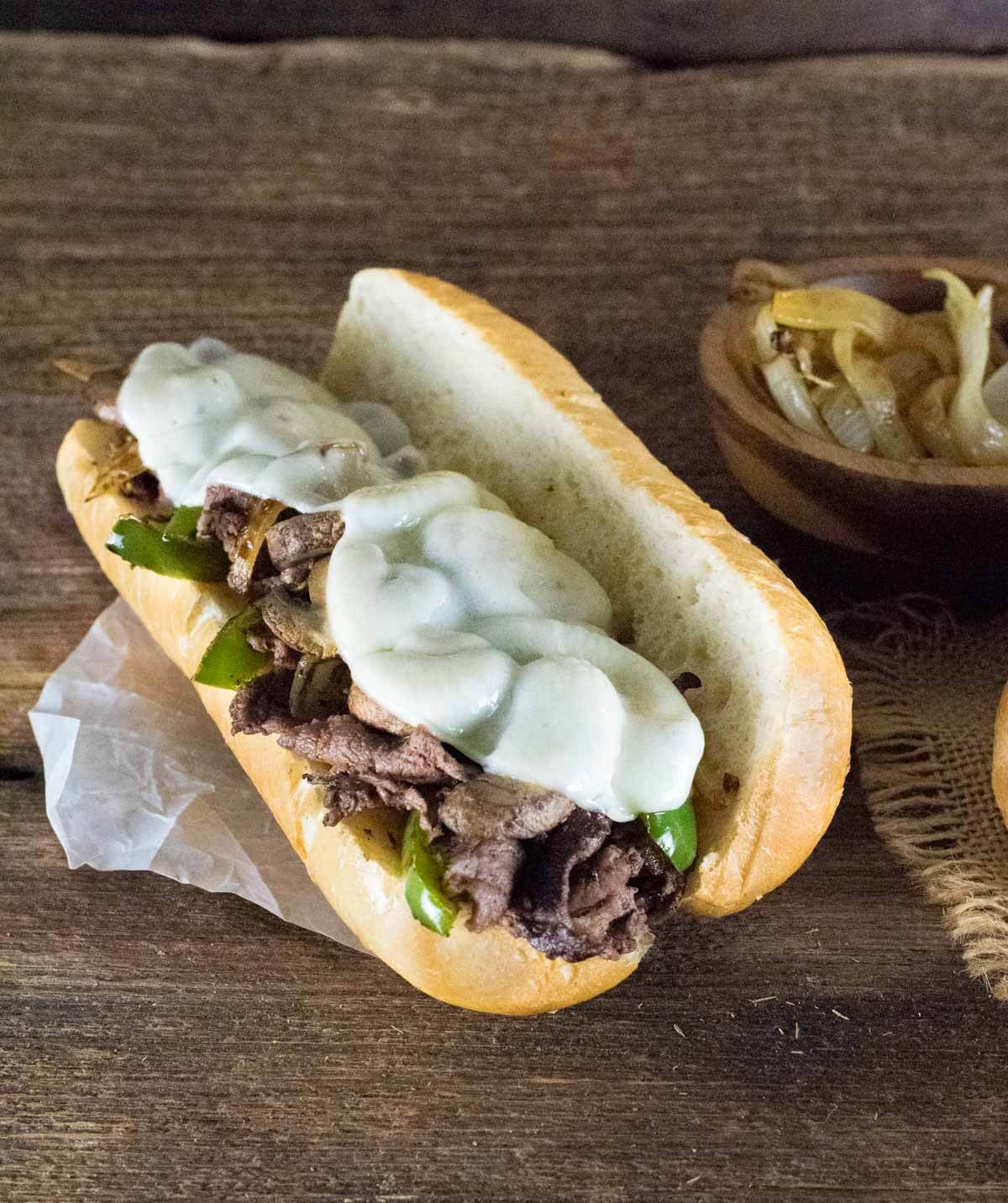 Venison sandwich topped with melted cheese, peppers, and onions.