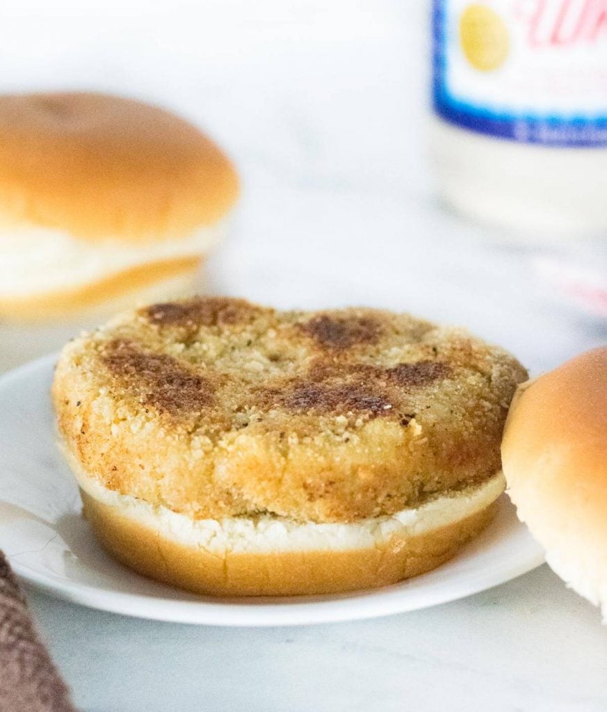 Breaded chicken patty on bottom bun sitting on white plate.